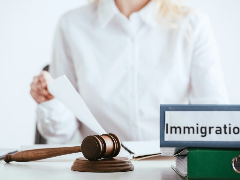 selective focus of gavel near folders with immigration law lettering with woman on background