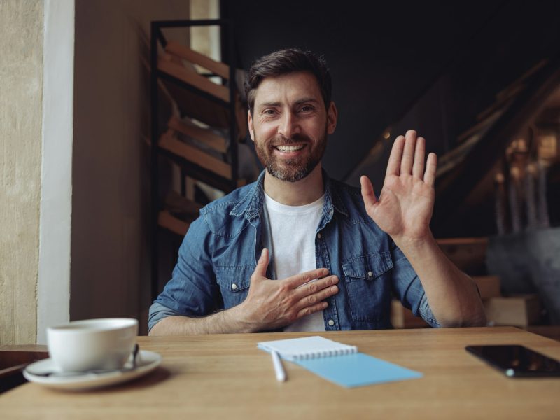 Young handsome man with hand on chest, making oath promise gesture in cafe. Promissing concept