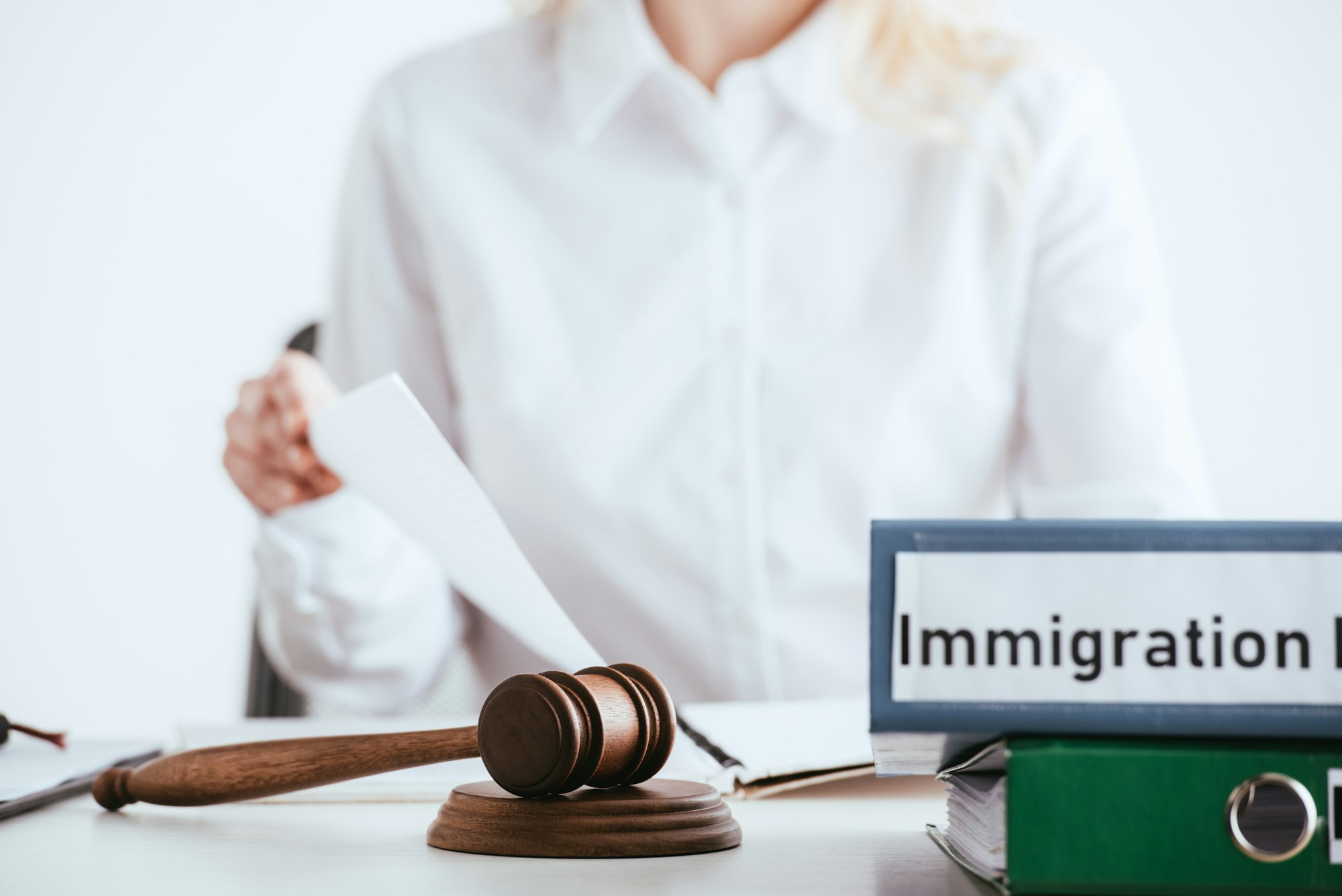 selective focus of gavel near folders with immigration law lettering with woman on background